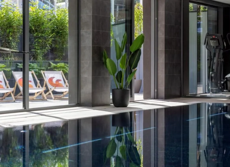 Przeszklona ściana basenu wychodzi na zielony ogród