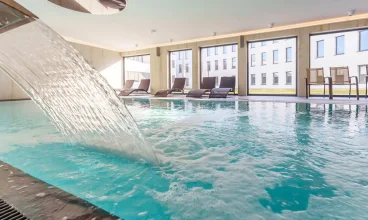 W basenie jest kaskada do hydromasażu, obok stoją leżaki